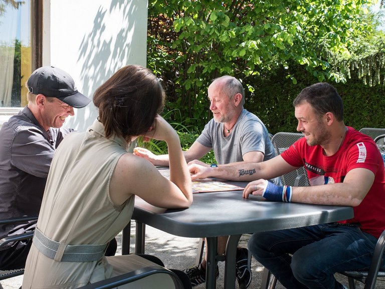 eine Frau und drei Männer sitzen am Gartentisch und spielen ein Brettspiel