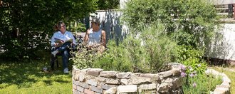 Steingarten mit kleinem Teich: im Hintergrund eine Frau und ein Mann auf einer Bank unterhalten sich