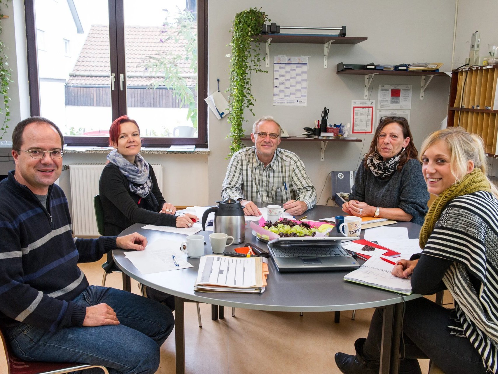 Mitarbeiter: drei Frauen und zwei Männer sitzen an einem runden Besprechungstisch im Büro