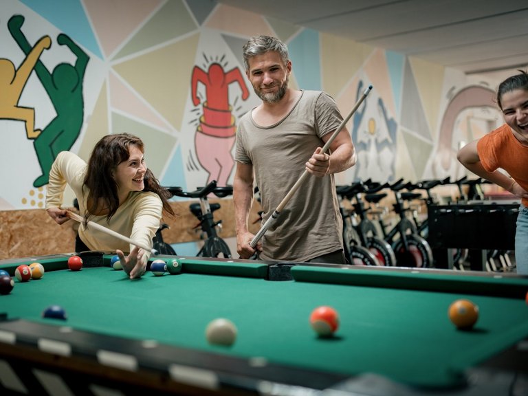 Zwei Frauen und ein Mann spielen lachend Billiard.