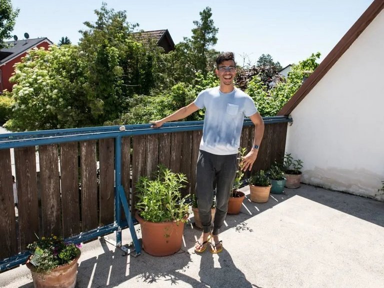 Ein junger Mann mit Brille, Jogginghose und Flip-Flops staht auf der Dachterasse