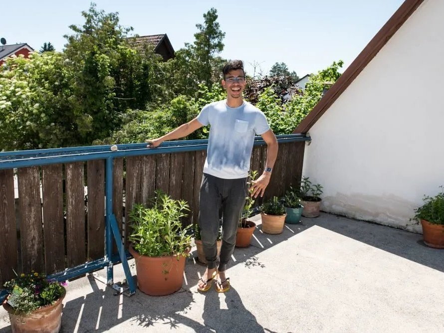 Ein junger Mann mit Brille, Jogginghose und Flip-Flops staht auf der Dachterasse