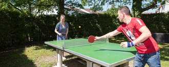 eine junge Frau und ein junger Mann im Garten beim Tischtennis